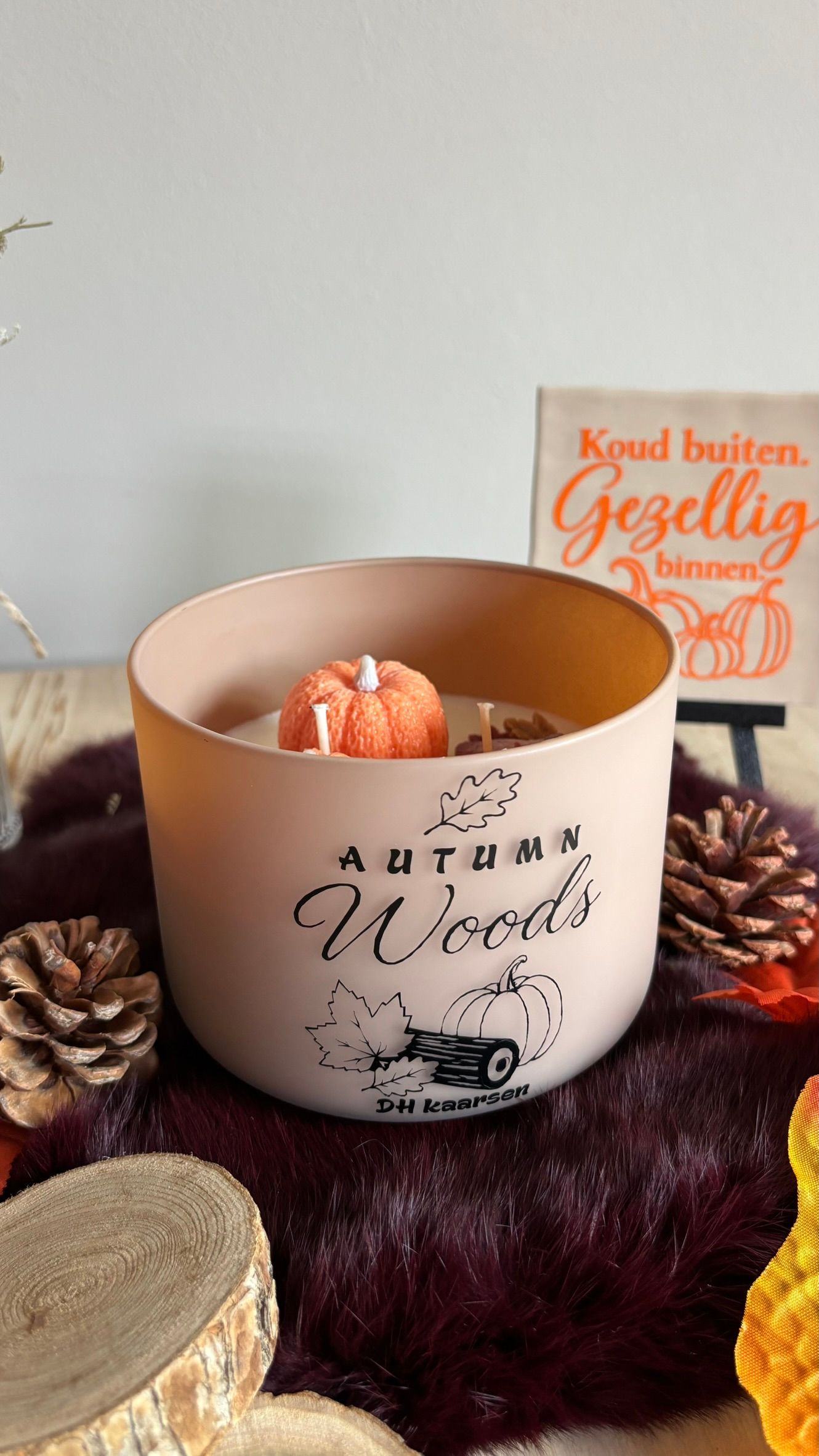 Een herfstdecoratie met kaarsen, gedroogde bloemen, bladeren en een klein houten bordje op een tafel.