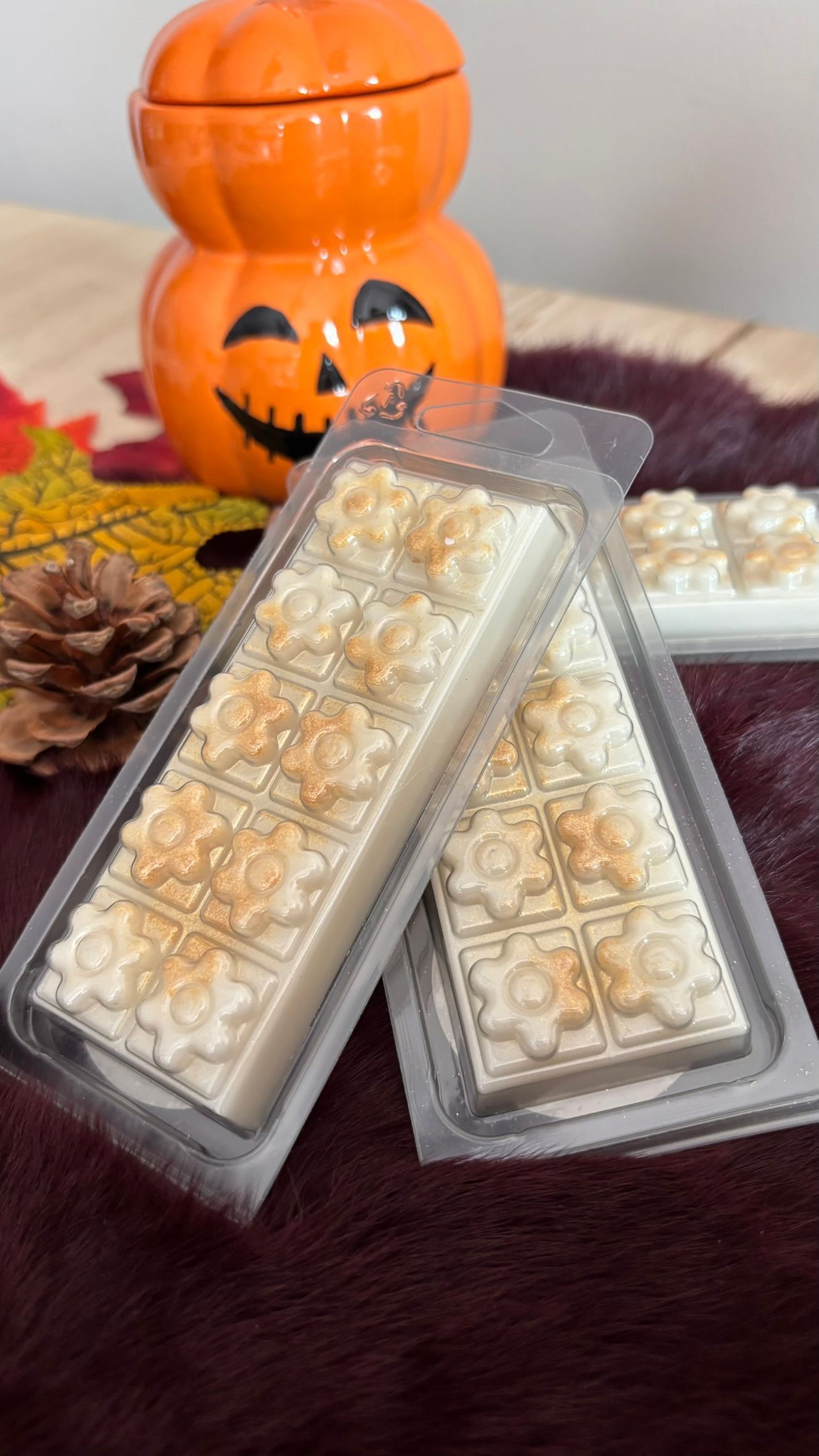 Halloween-pompoendecoratie achter twee doorzichtige schalen met witte en gouden snoepjes op een bordeauxrode ondergrond.