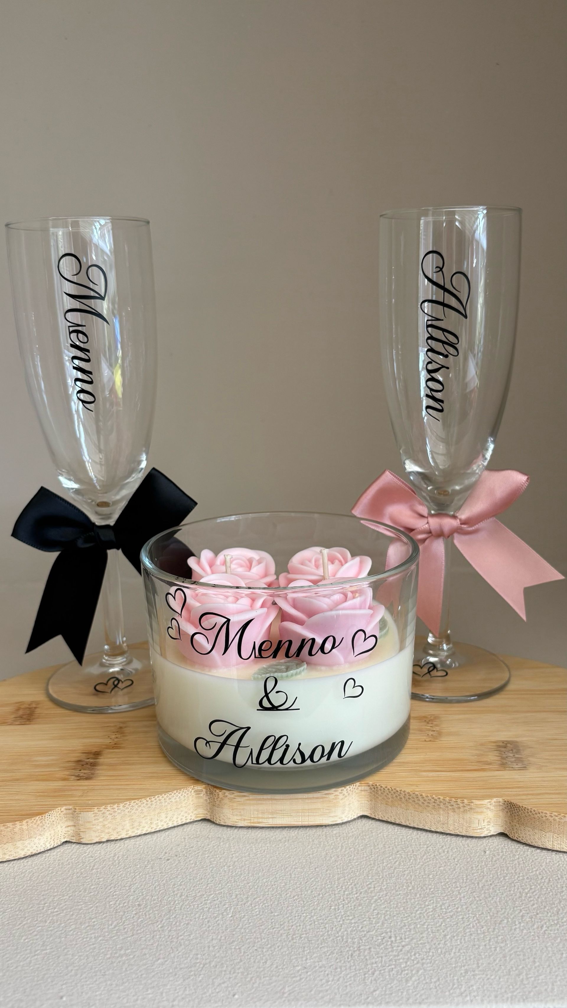 Champagneglazen voor de bruiloft en een bloemstuk met kaarsen, roze rozen en zwarte en roze linten.
