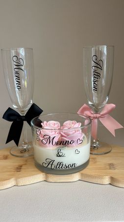 Champagneglazen voor de bruiloft en een bloemstuk met kaarsen, roze rozen en zwarte en roze linten.