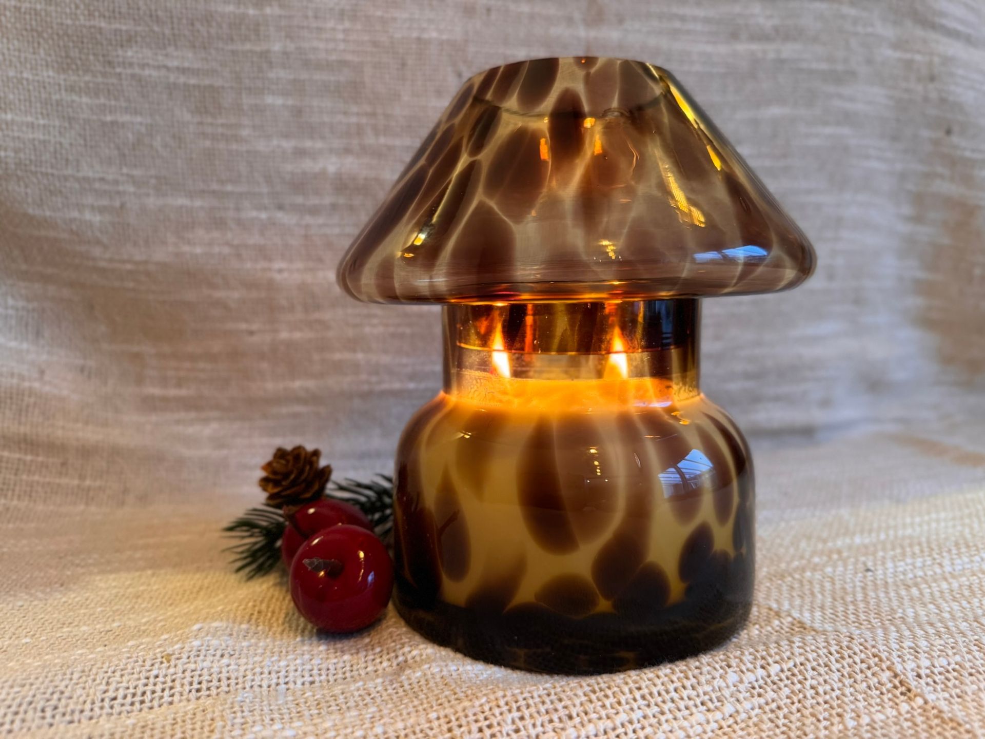 Een amberkleurige glazen paddenstoellamp gloeit op een tafel met dennentakjes en rode bessen.