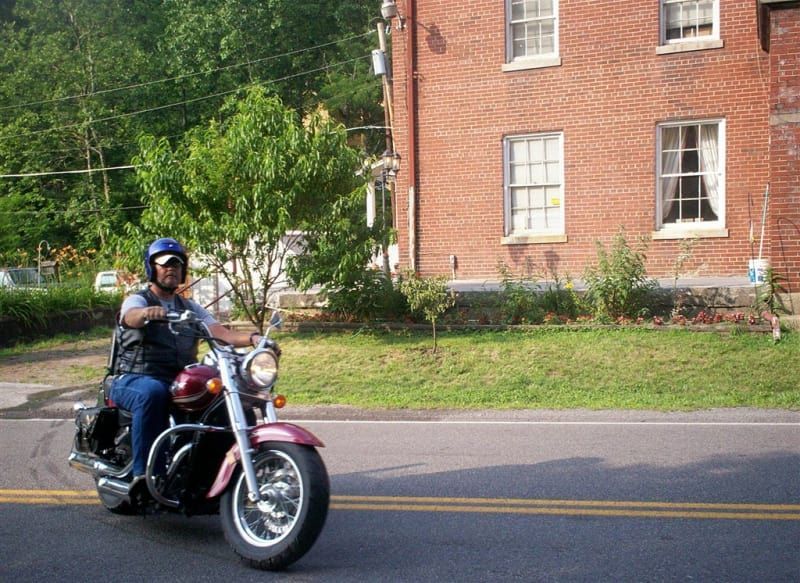 A man is riding a motorcycle down a road in front of a brick building