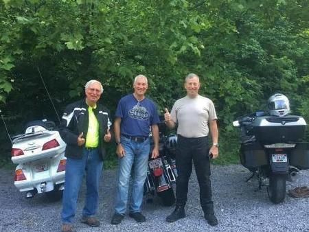 Three men are standing next to motorcycles and giving a thumbs up.