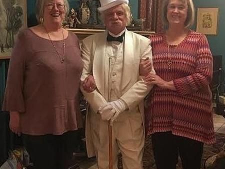 A man in a tuxedo and top hat is standing next to two women.