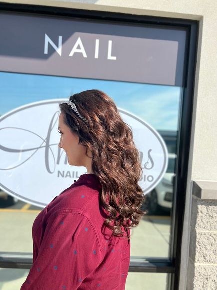 Woman with wavy brown hair, wearing a headband, stands in front of a nail salon window.
