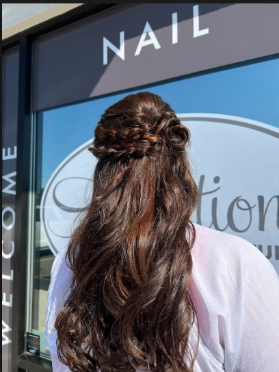 Person with long brown hair seen from behind outside a nail salon with a “Welcome” sign.