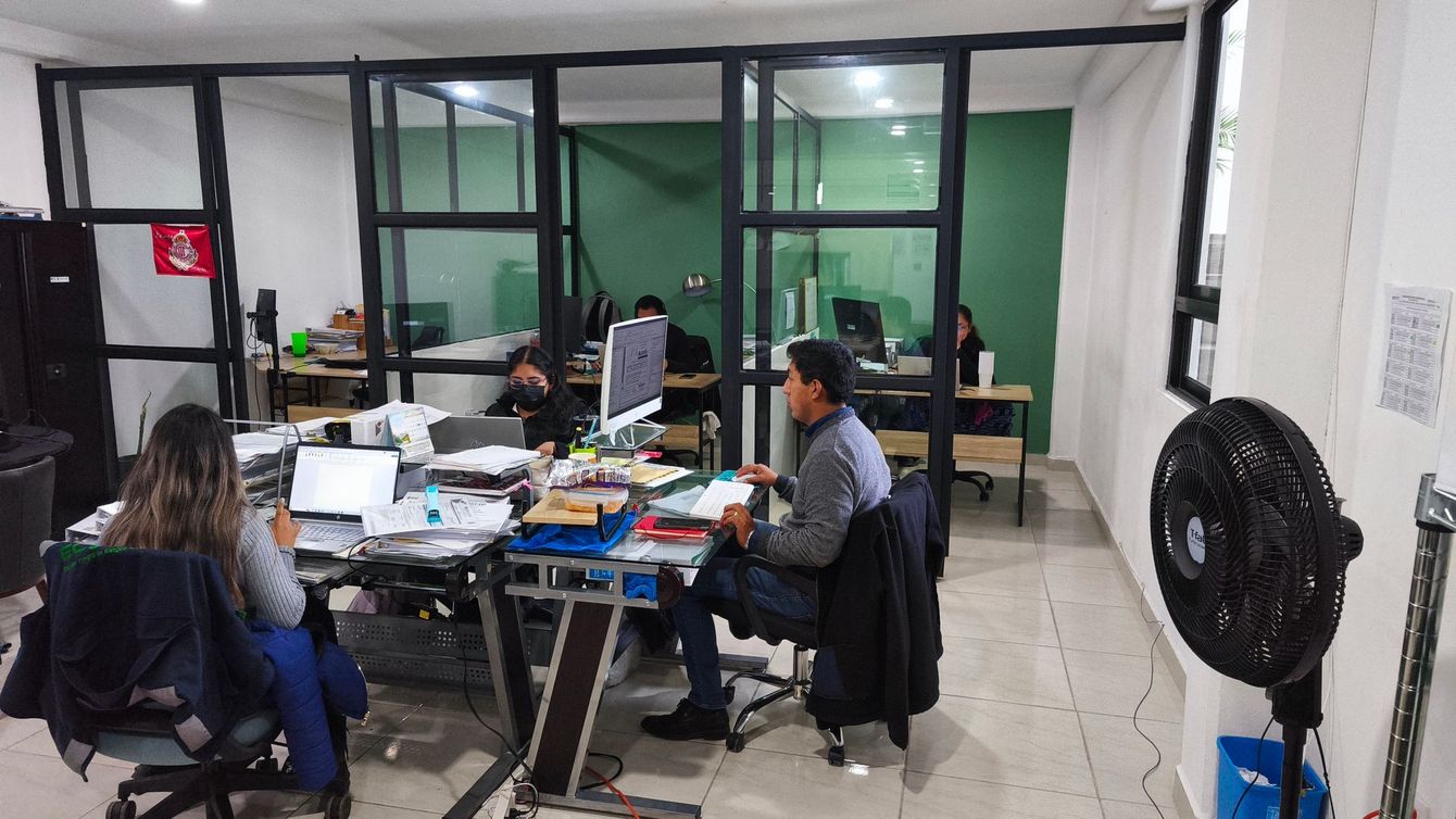 Oficina de ECOSHE con gente en escritorios, algunos trabajando con computadoras.