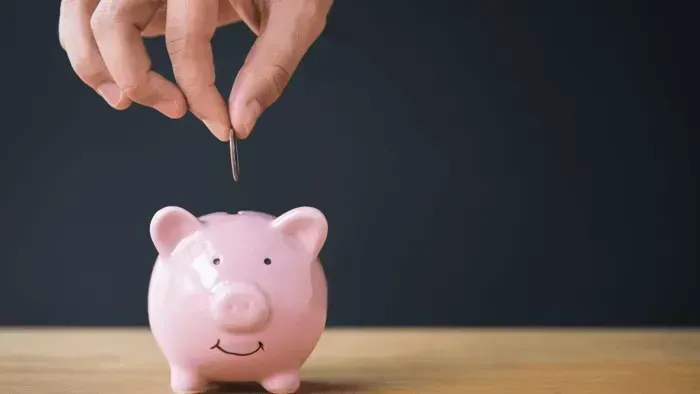 Hands placing a coin into a pink piggy bank on a table