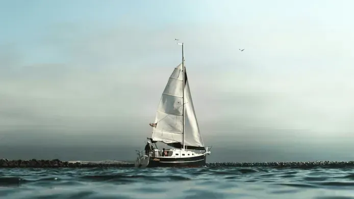Sailboat with white sails gliding on calm water near a rocky breakwater at dusk