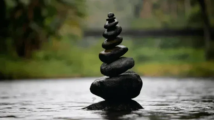 Stacked black stones balanced in a tranquil stream with a blurred green background