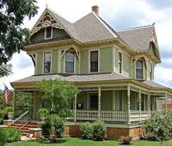 A large green house with a large porch and an american flag on the front.
