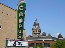 A large green sign with the word campus on it is in front of a building.
