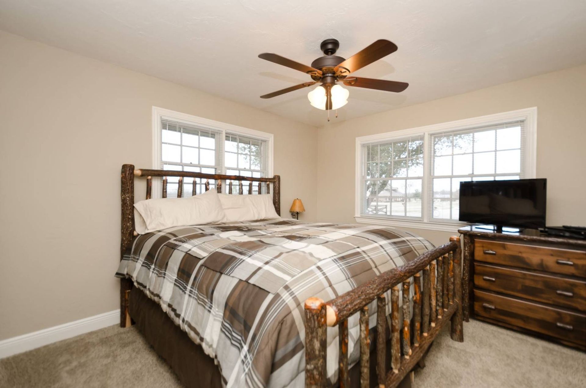 A bedroom with a bed , dresser , television and ceiling fan.