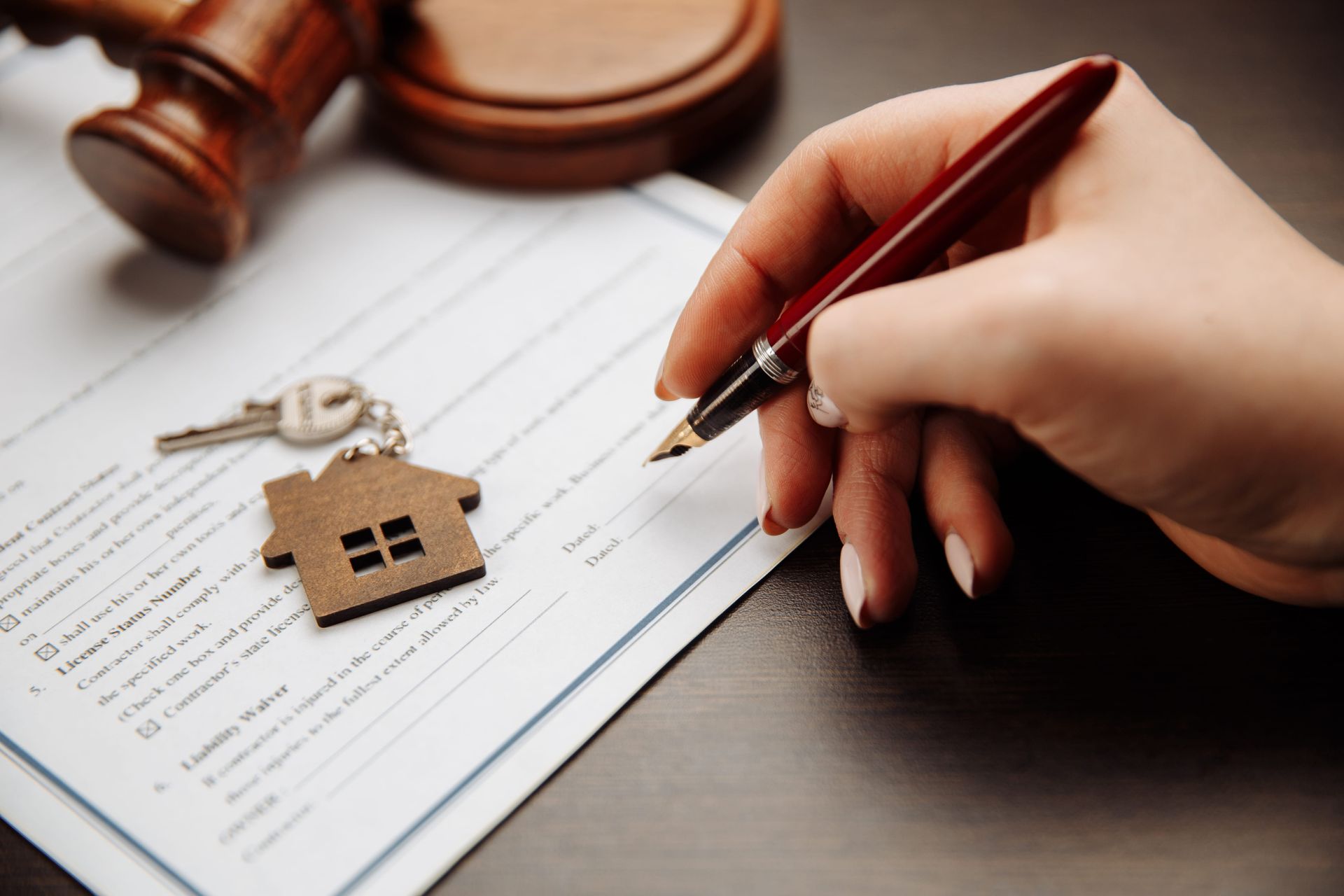 Hand signing a real estate document beside a house key and gavel