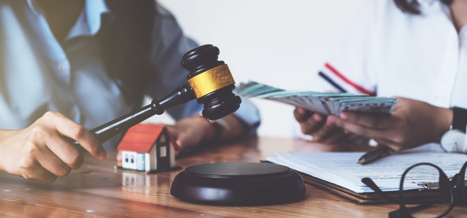 Judge’s gavel beside a small house model as a person signs paperwork, suggesting a property/legal sale.