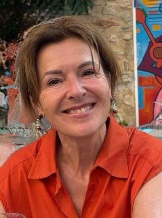 Een lachend persoon in een oranje shirt voor een kleurrijke muurschildering en een stenen muur.
