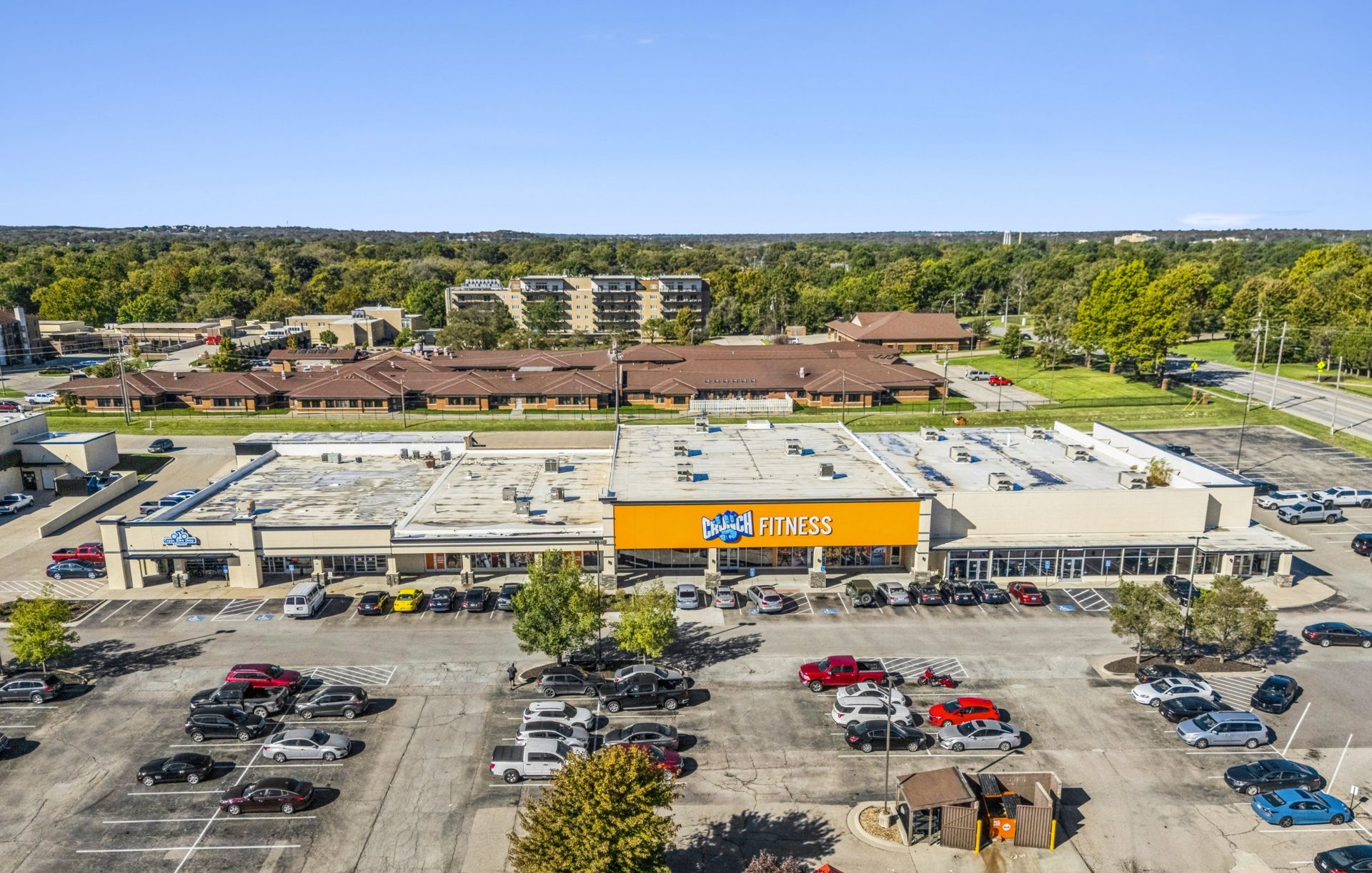 Aerial view of a busy parking lot and shopping center with a large orange store sign in front of trees.