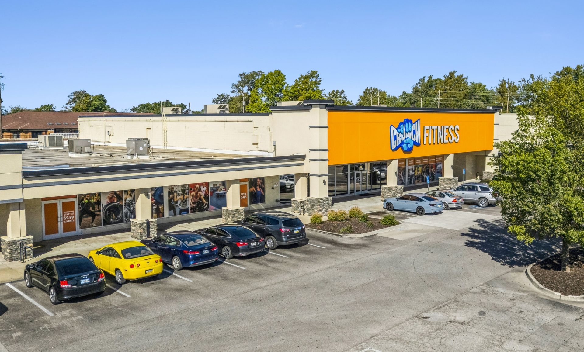 A storefront shopping center with parked cars and an orange sign over the entrance.