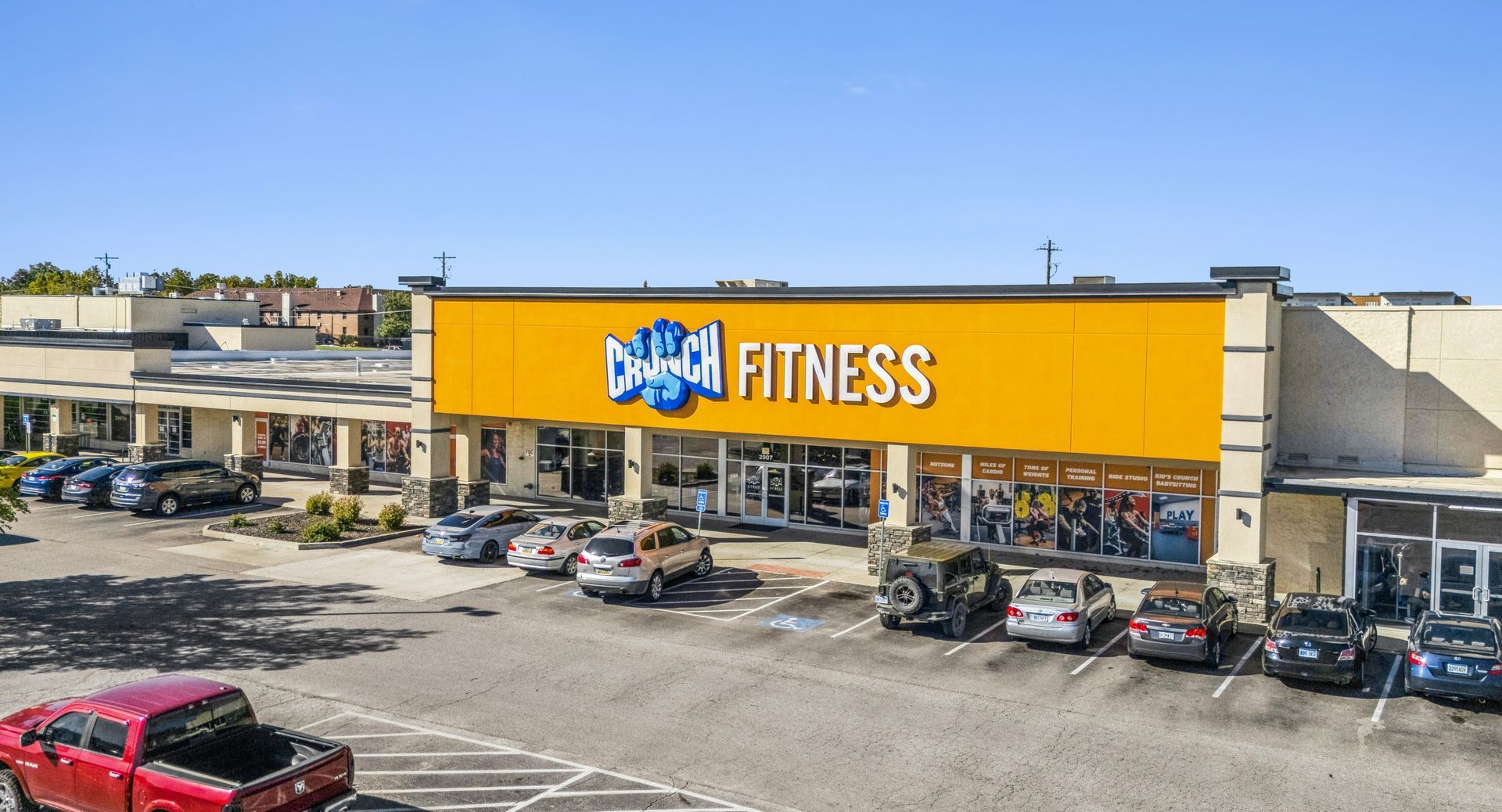 Storefront of UFC Gym with a bright yellow sign in a strip mall parking lot