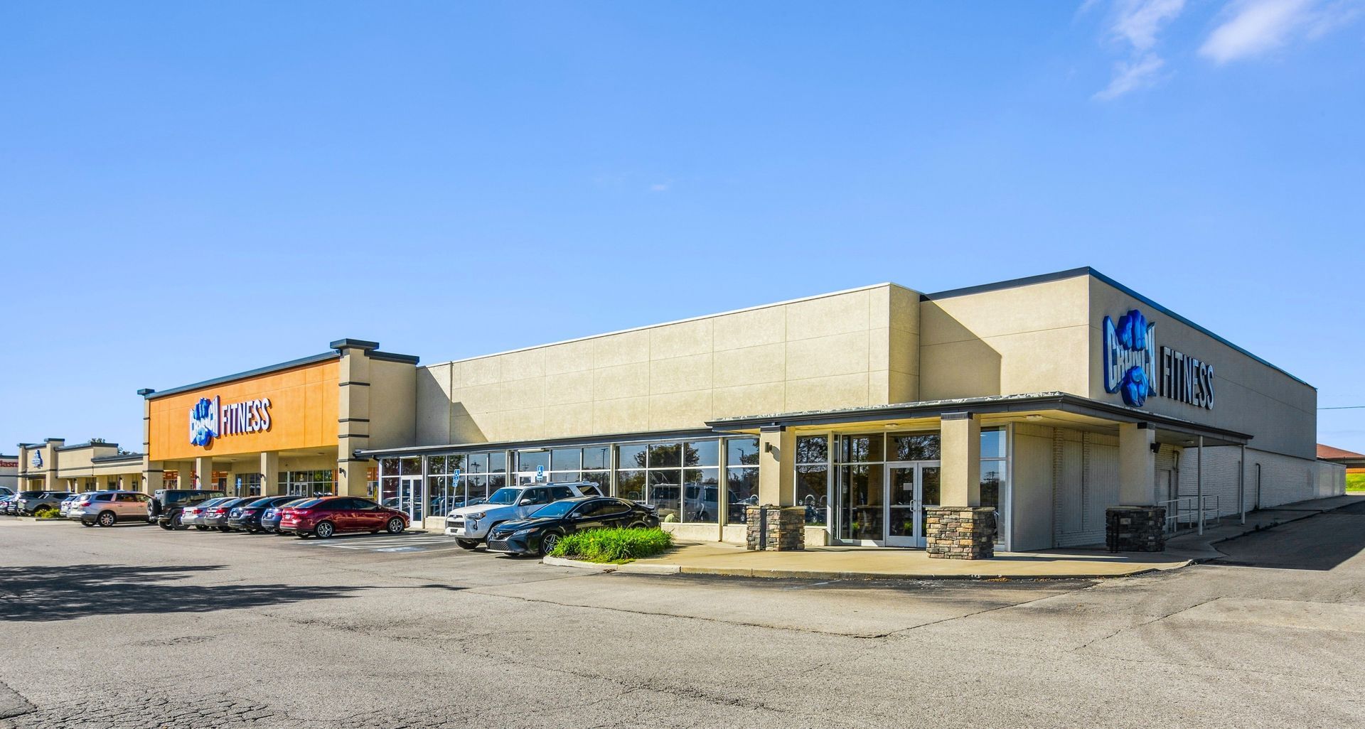 Large beige shopping plaza with parked cars under a clear blue sky