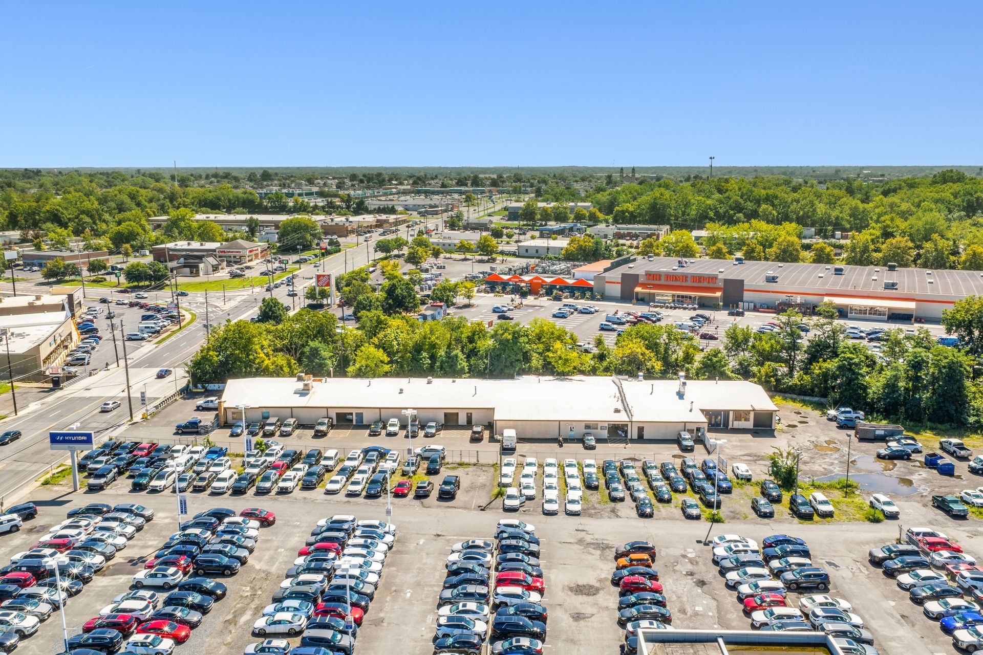 Aerial view of a busy parking lot beside a Caliber Collision and tree-lined streets under a clear sky