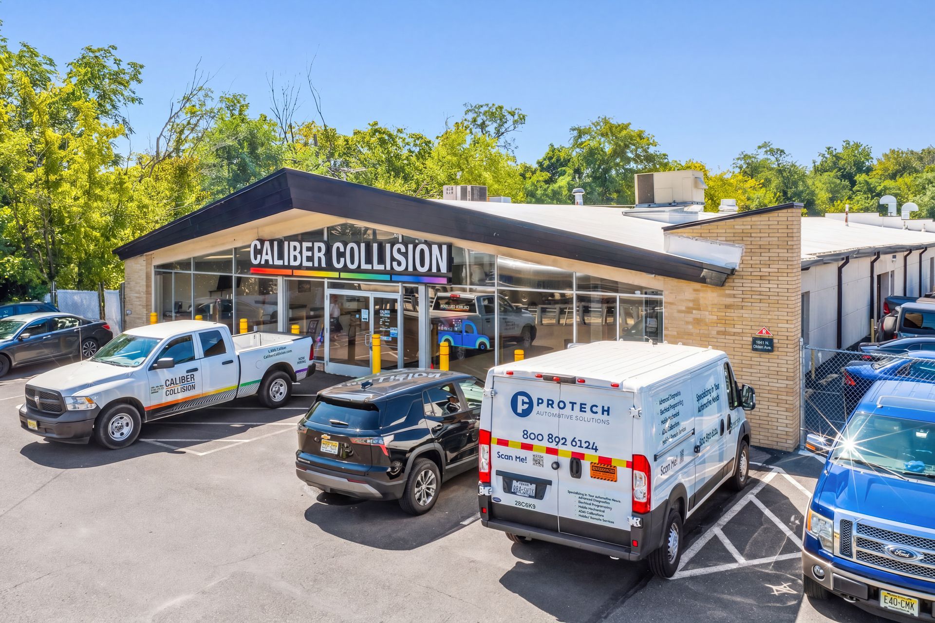 Caliber Collision repair shop with service trucks parked outside on a sunny day