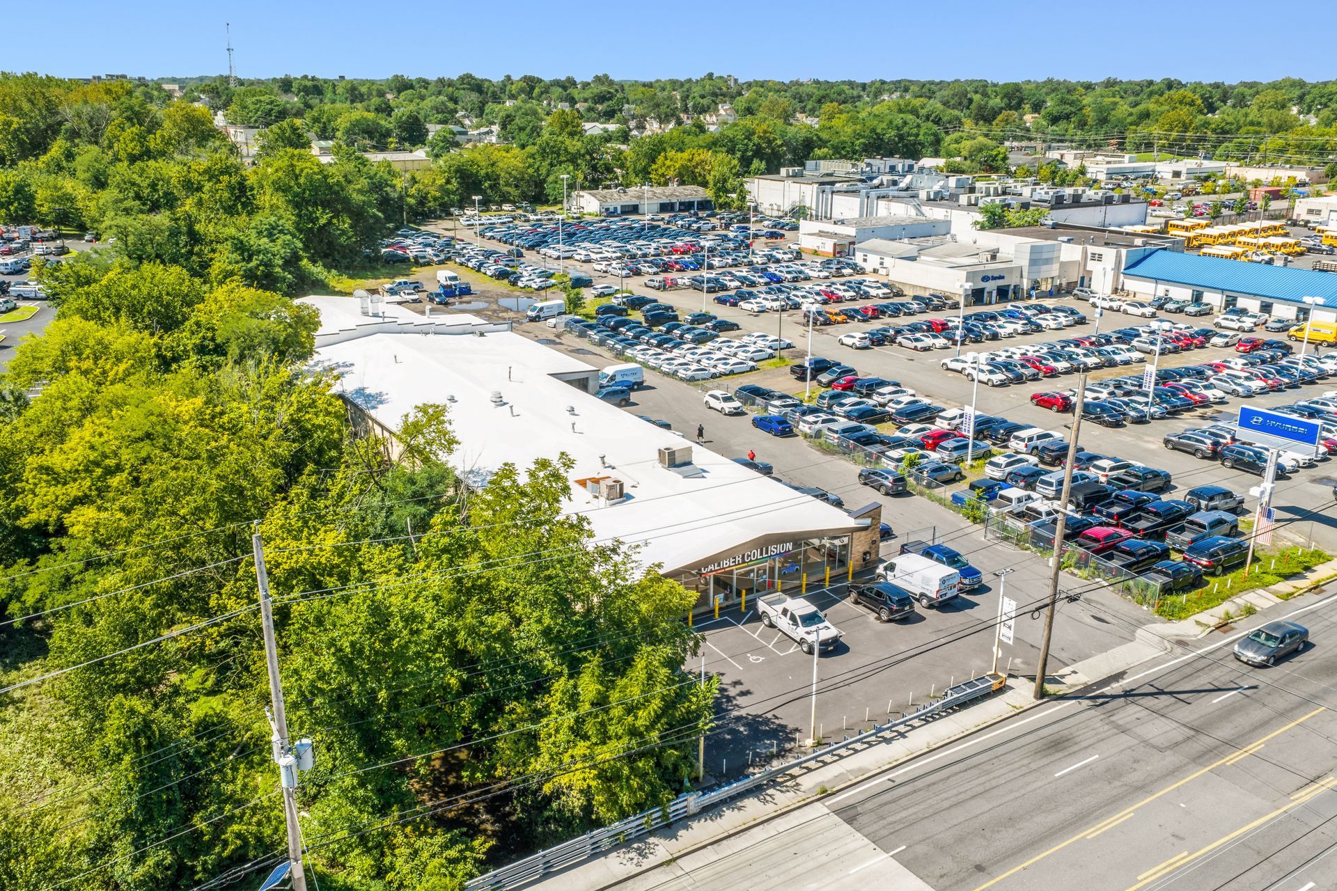 Aerial view of a crowded parking lot beside white-roofed Caliber Collision and tree-lined streets
