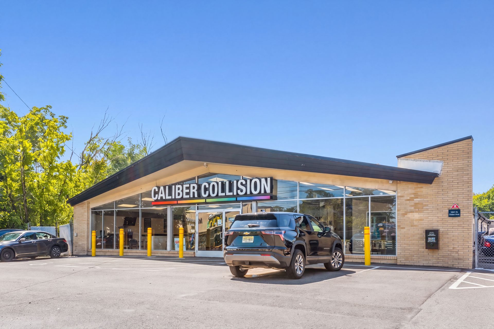 Caliber Collision auto repair shop with a black SUV parked outside under a blue sky