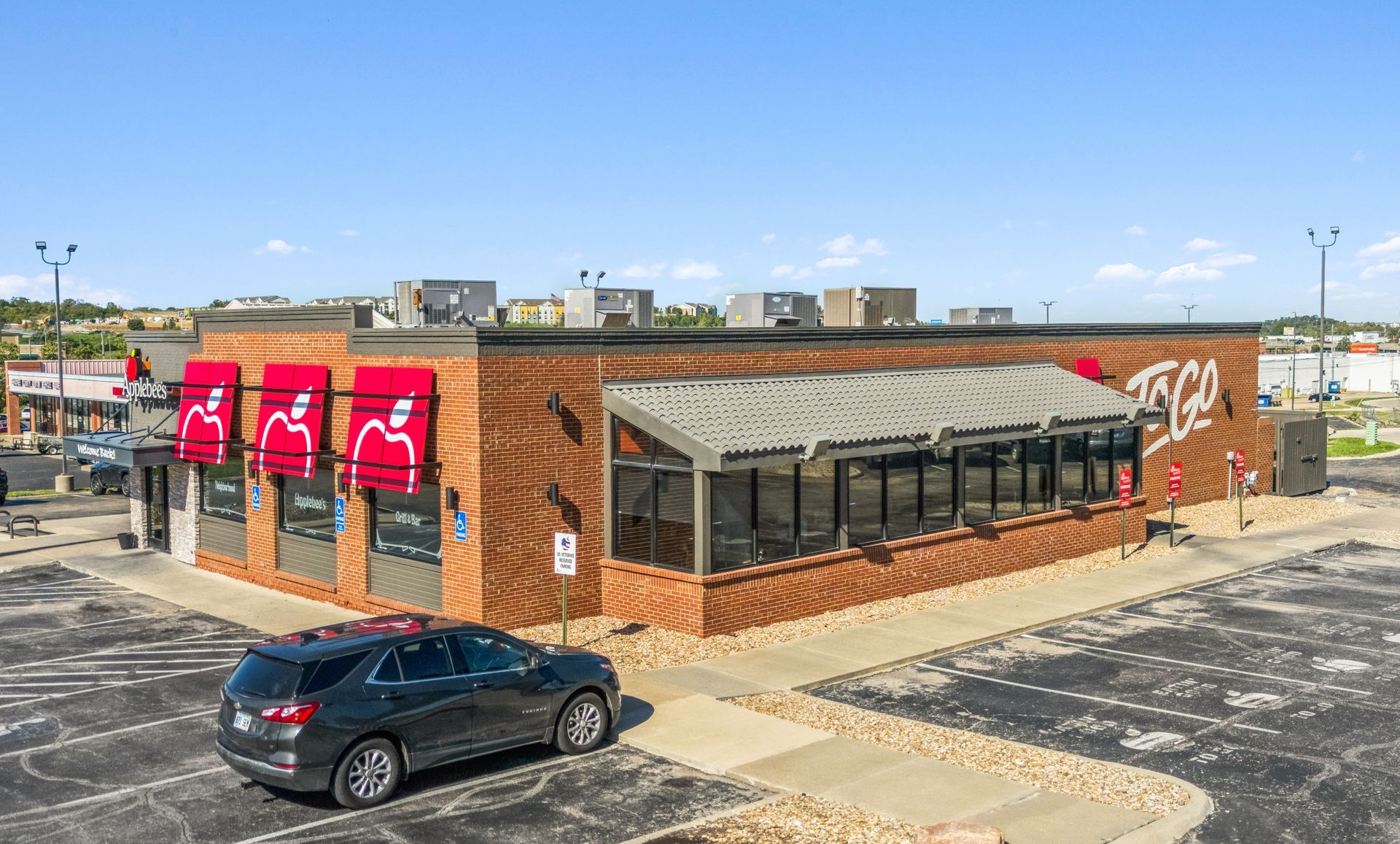 Brick fast-food restaurant with red signs on a corner lot, black car parked outside under a clear sky