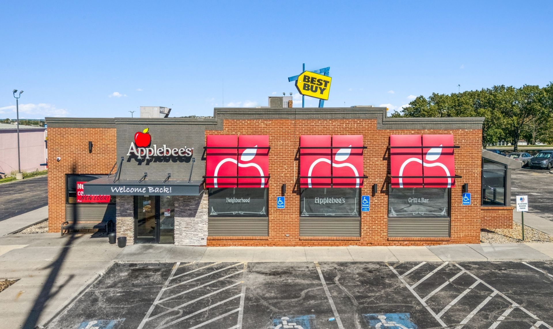Brick Applebees restaurant with red apple signs and empty parking lot under clear sky
