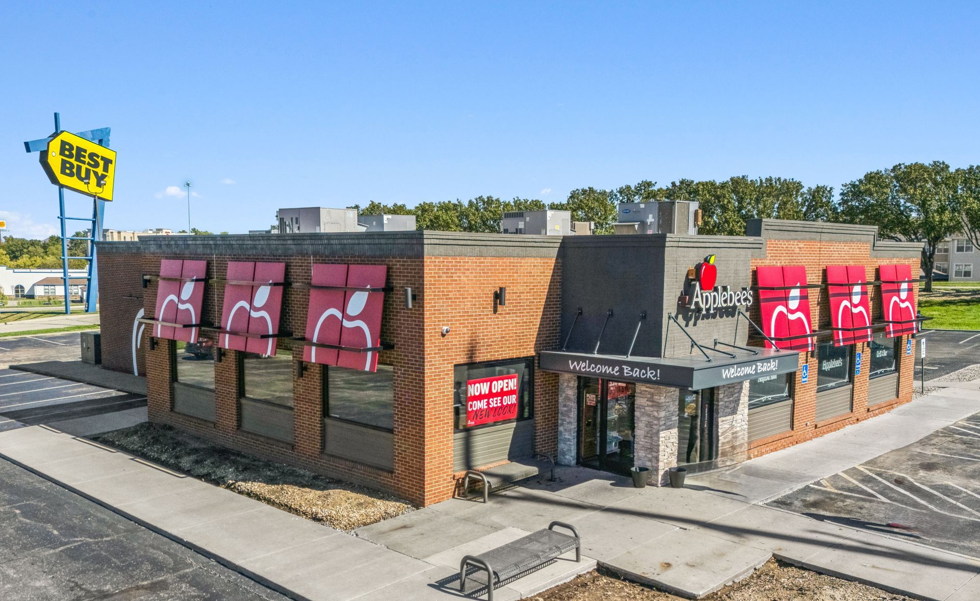 Small brick restaurant with red awnings and a bright yellow sign on a sunny street corner.