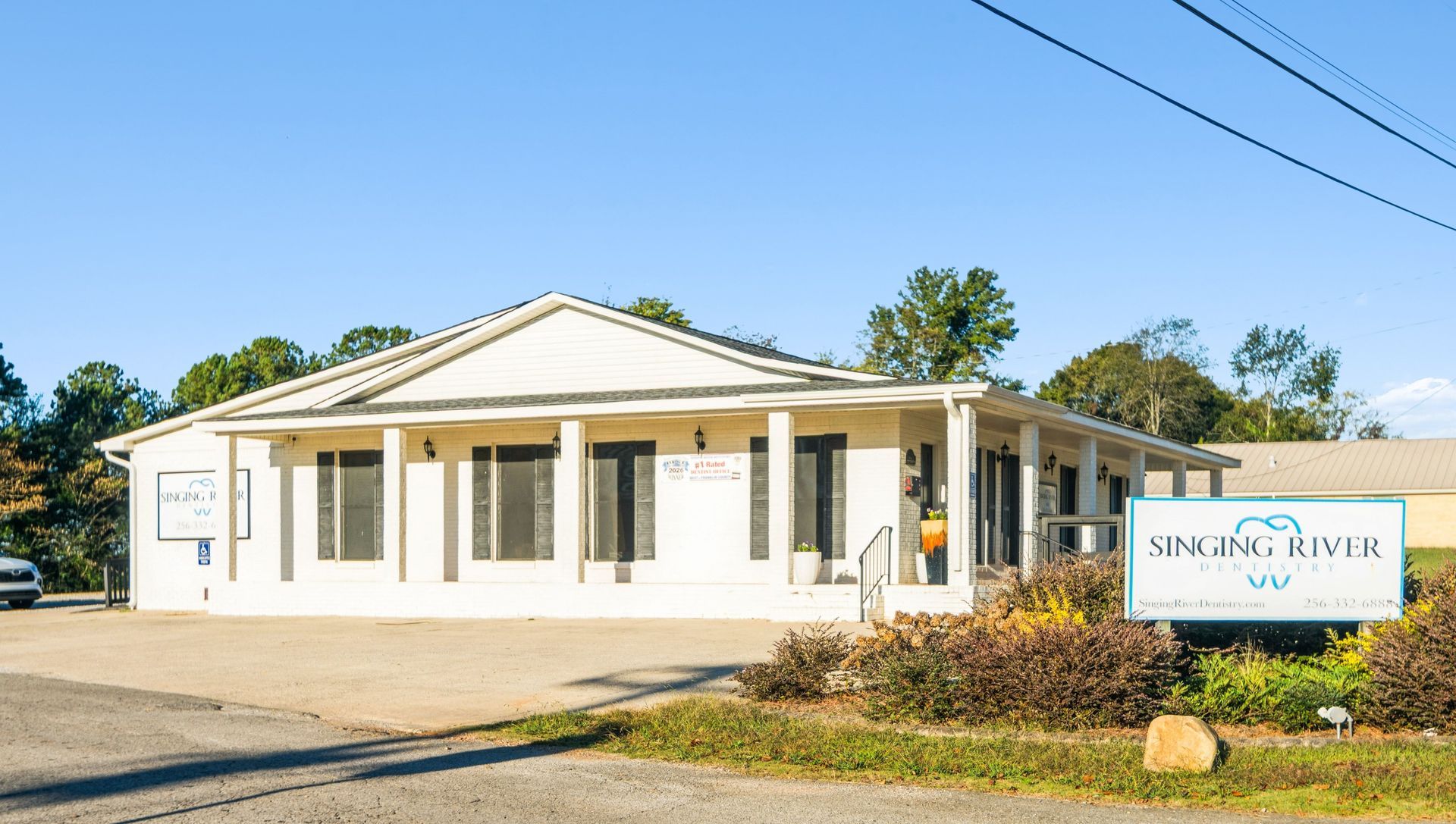 White single-story office building with a porch and sign in front under a clear blue sky