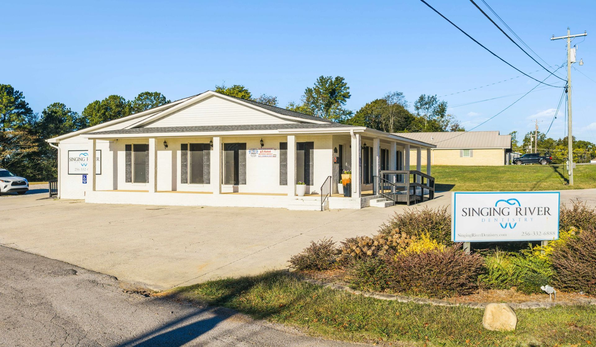 Small beige office building with a sign in front and a parking area on a sunny day