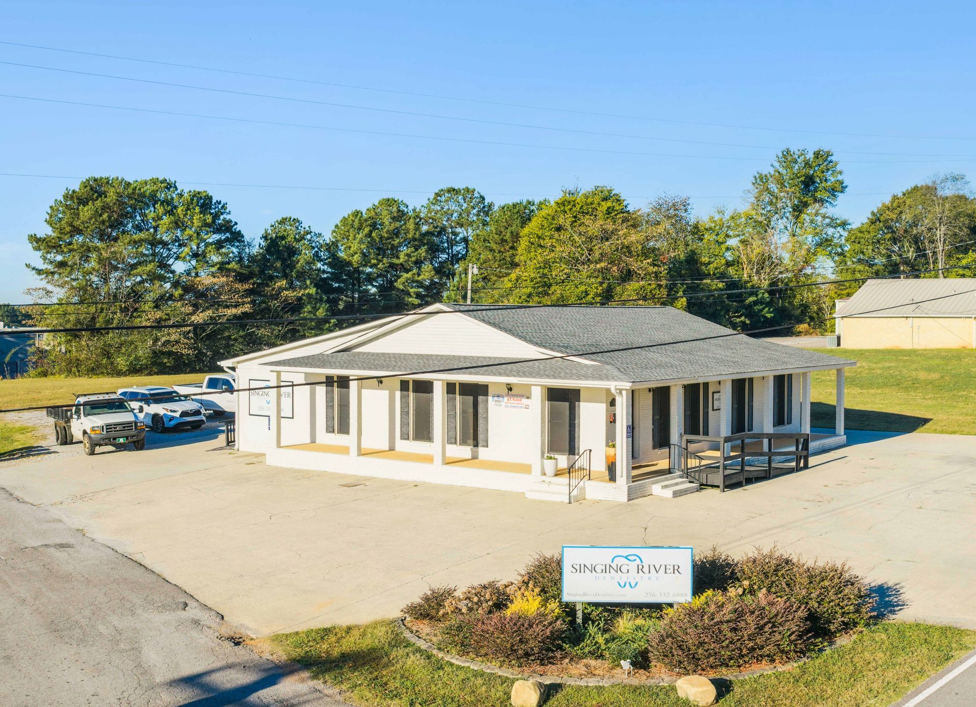 Single-story white office building with gray roof and parking lot in front