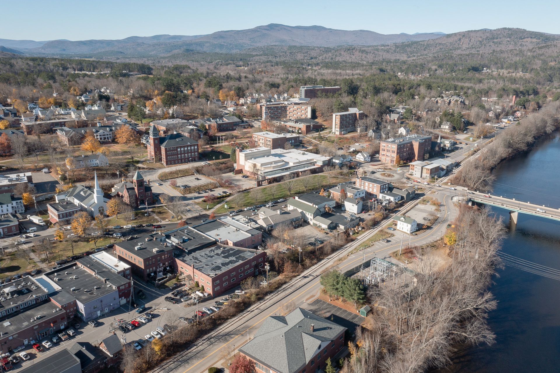 Aerial view of a town with brick buildings, a river, and mountains in the background.