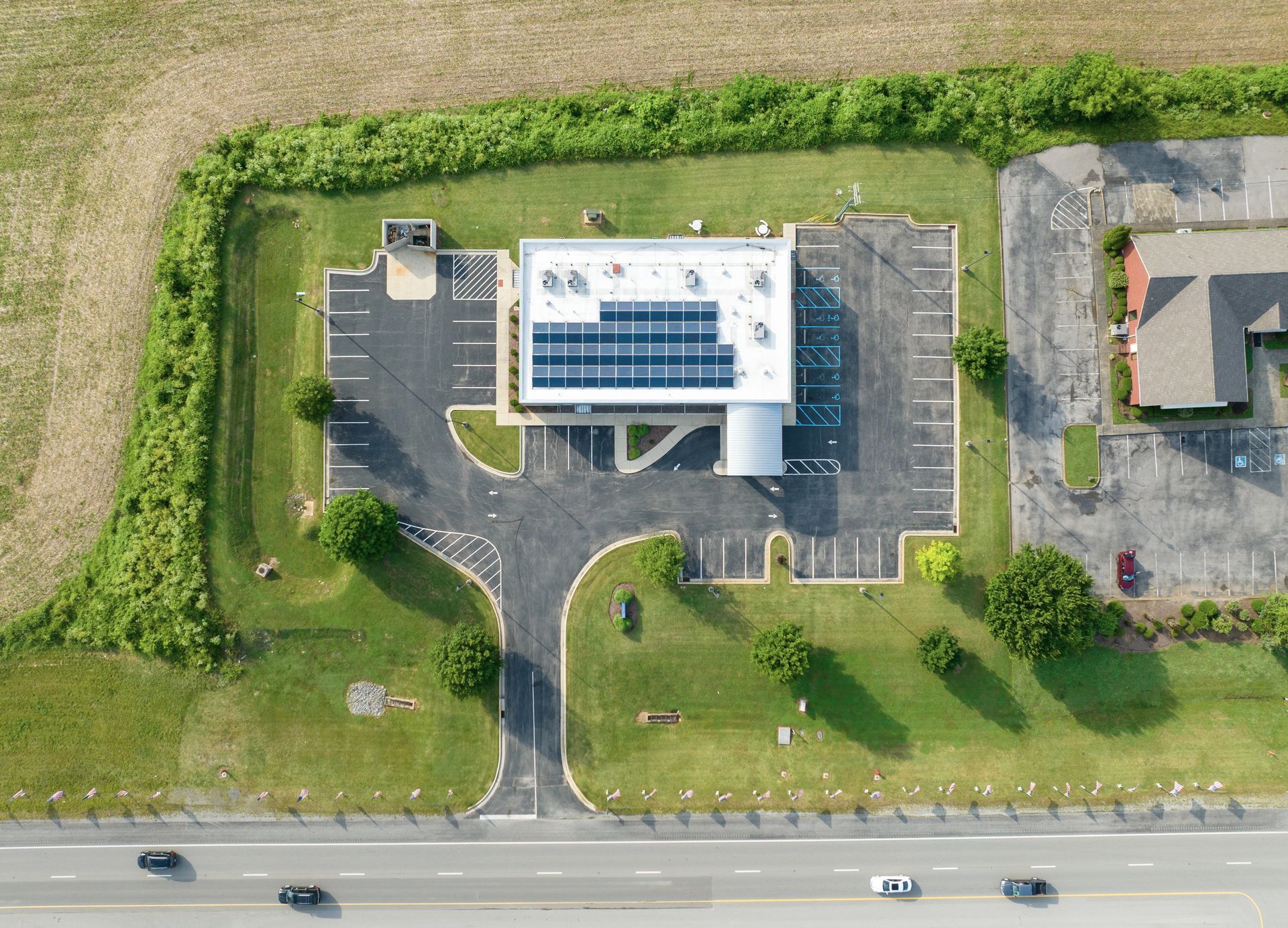 Aerial view of a Fresenius Medical Care building with solar panels, parking lot, and roadside greenery beside a highway.
