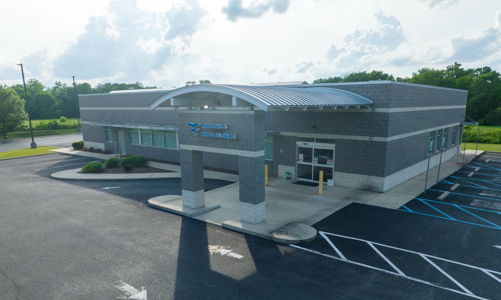 A Fresenius Kidney Care commercial building with a glass entrance and blue parking lines in front, viewed from above.