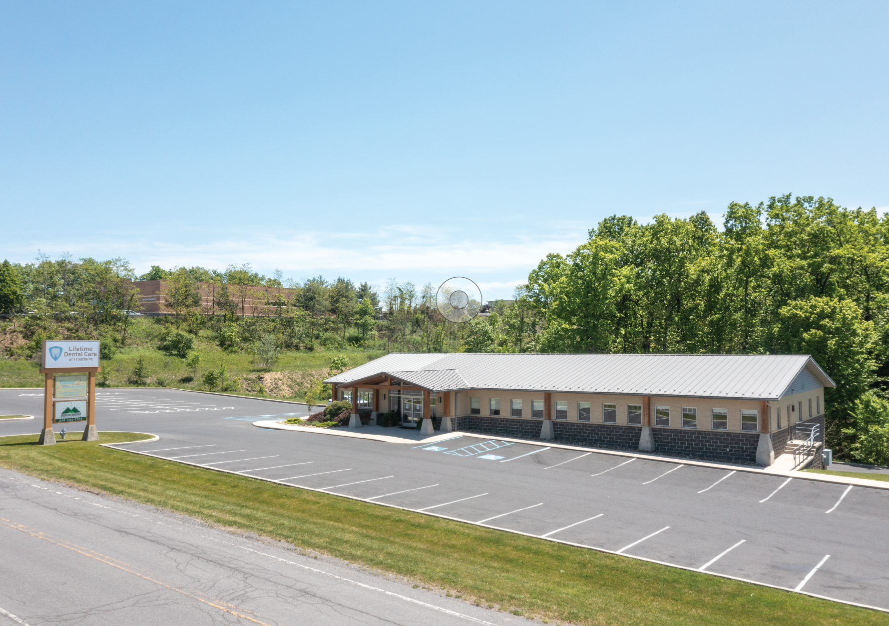 Parking lot beside a long single-story Heartland Dental commercial building with a sign and trees under a blue sky