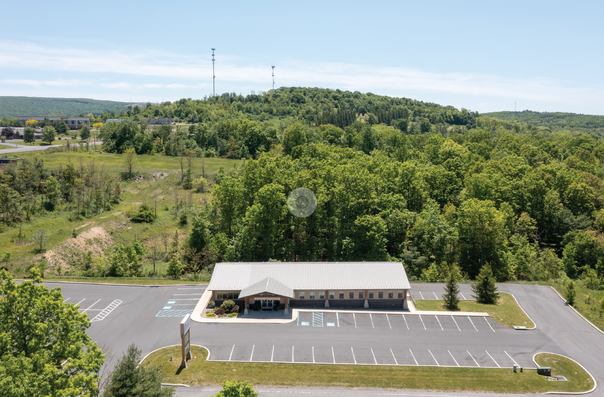 Aerial view of a Heartland Dental and Palaisa Orthodontics storefront with an empty parking lot beside a wooded hill under a clear sky