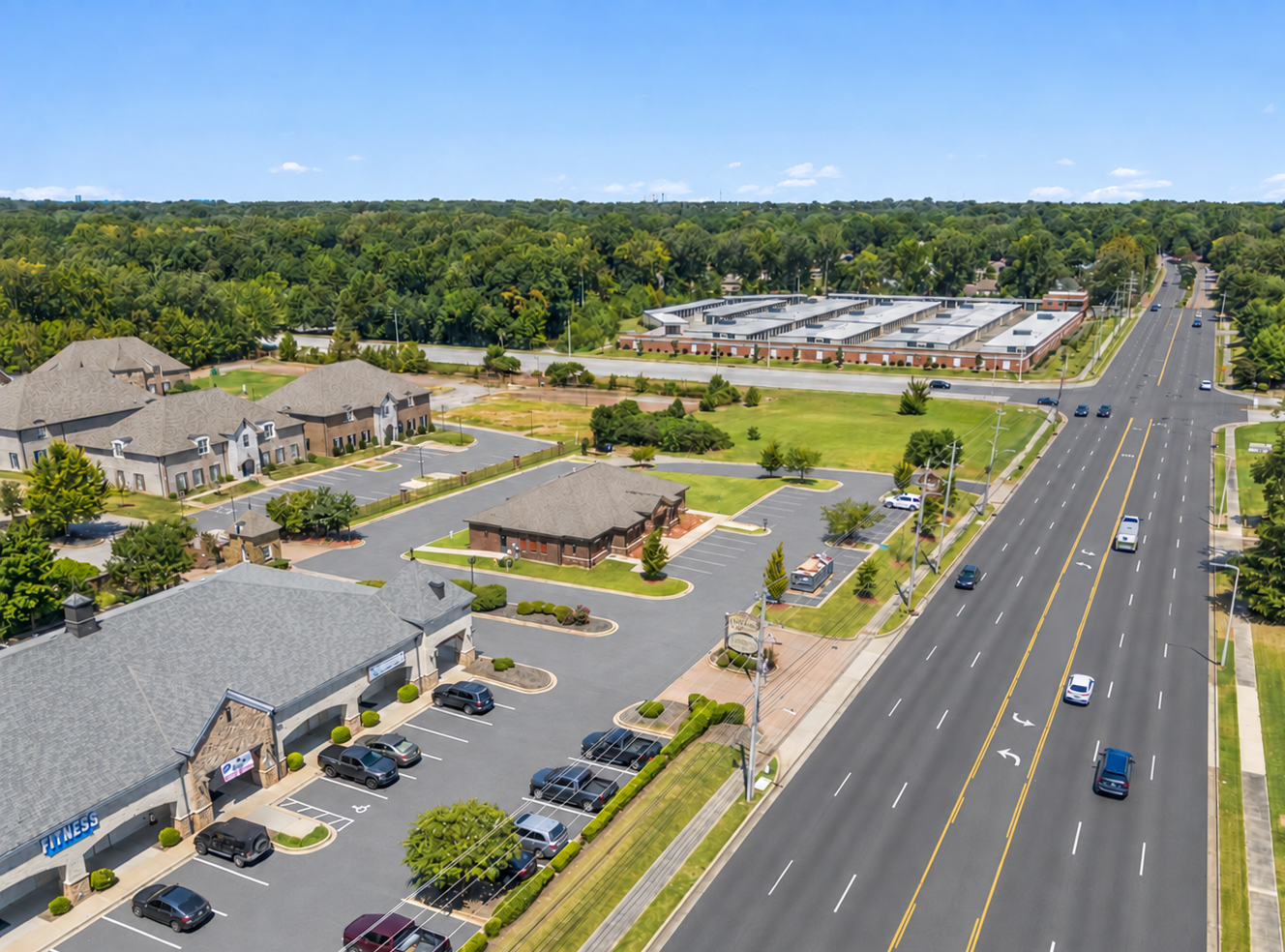 Aerial view of a suburban apartment complex beside a busy multi-lane road and parking lots.