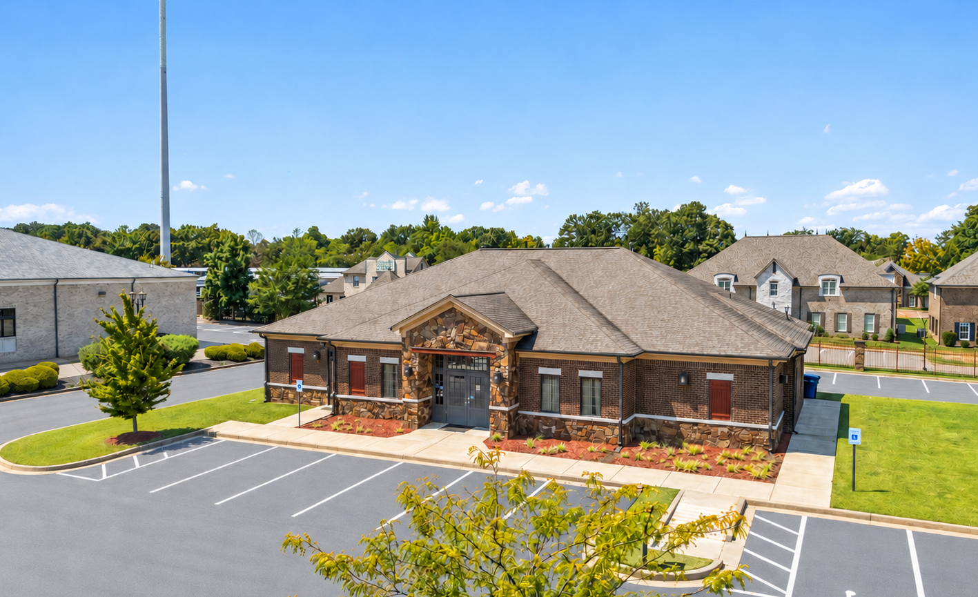 Aerial view of a brick office building with a parking lot and landscaped grounds on a sunny day