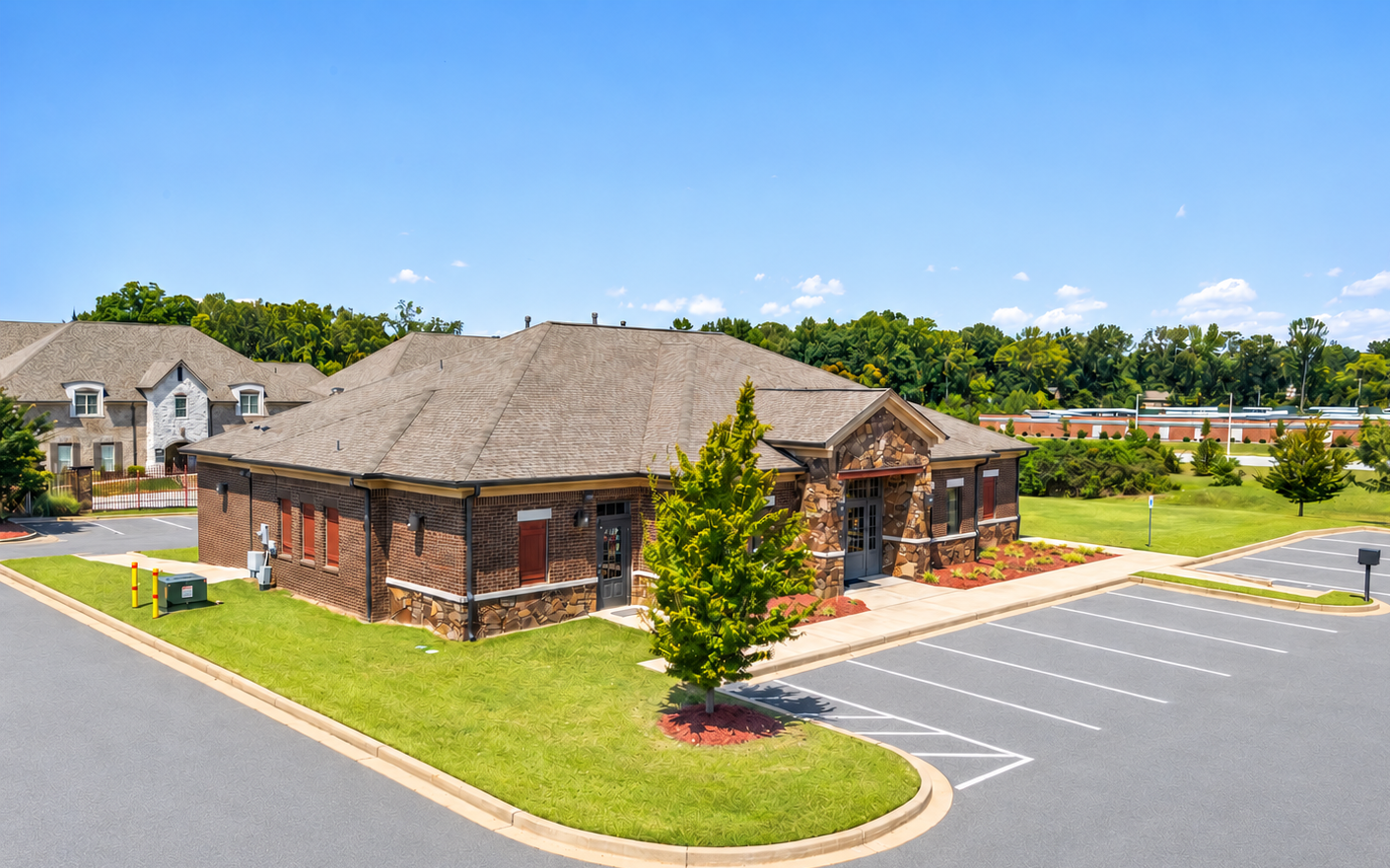 Brick office building with a shingled roof, parking lot, and landscaped lawn on a sunny day
