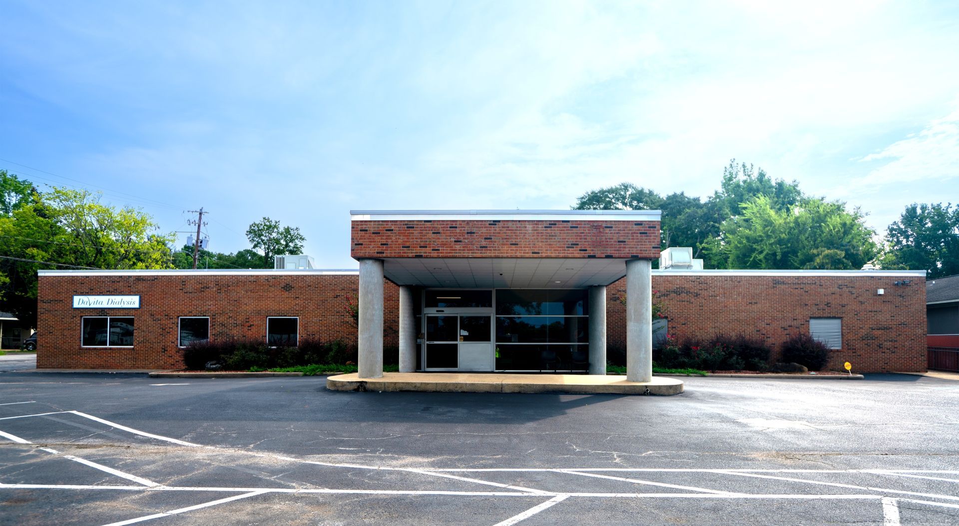 Brick DaVita Dialysis NNN medical office building with a central covered entrance and empty parking lot in front