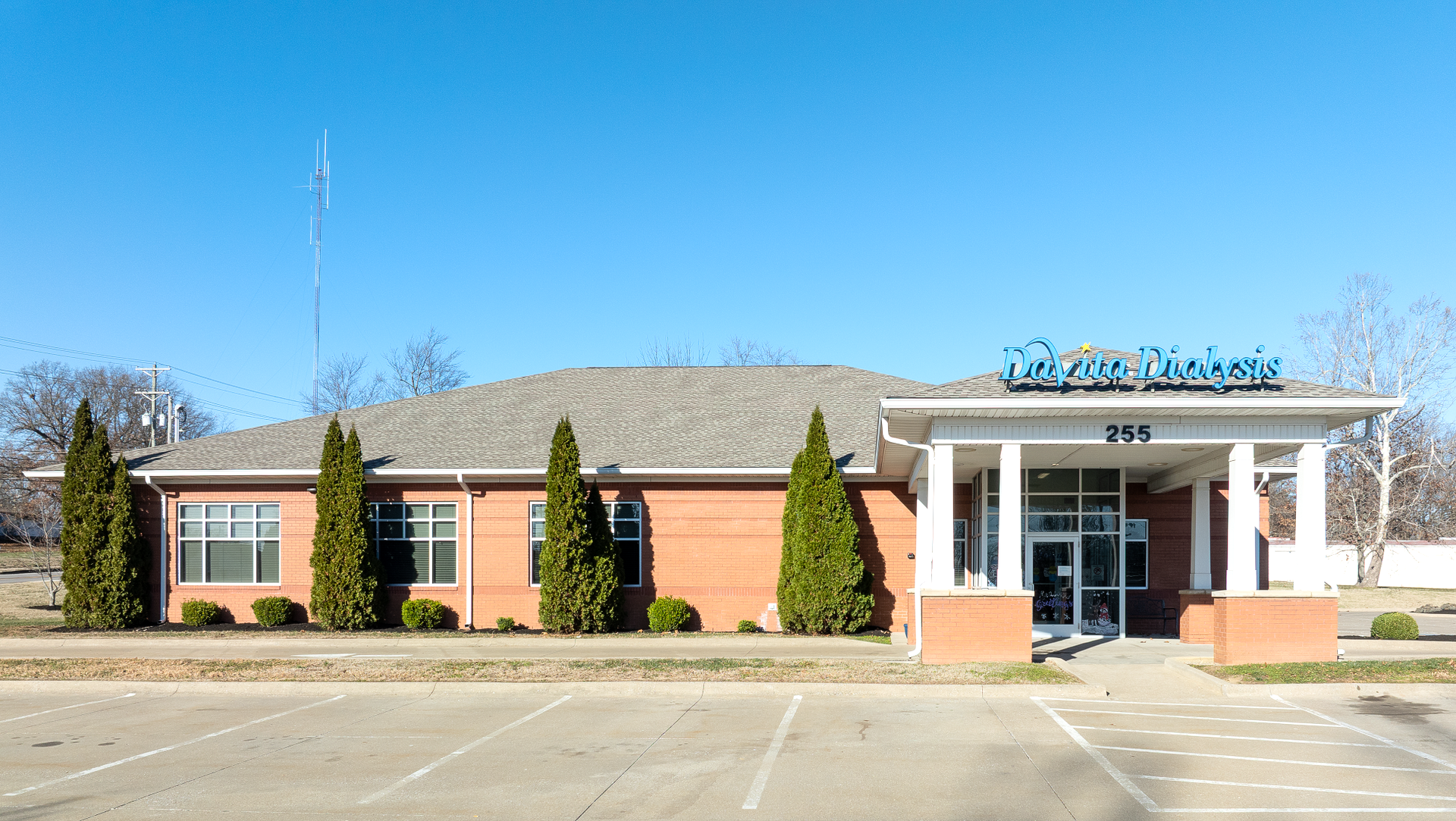Net lease davita medical building with blue sign, tall trees, and clear sky.