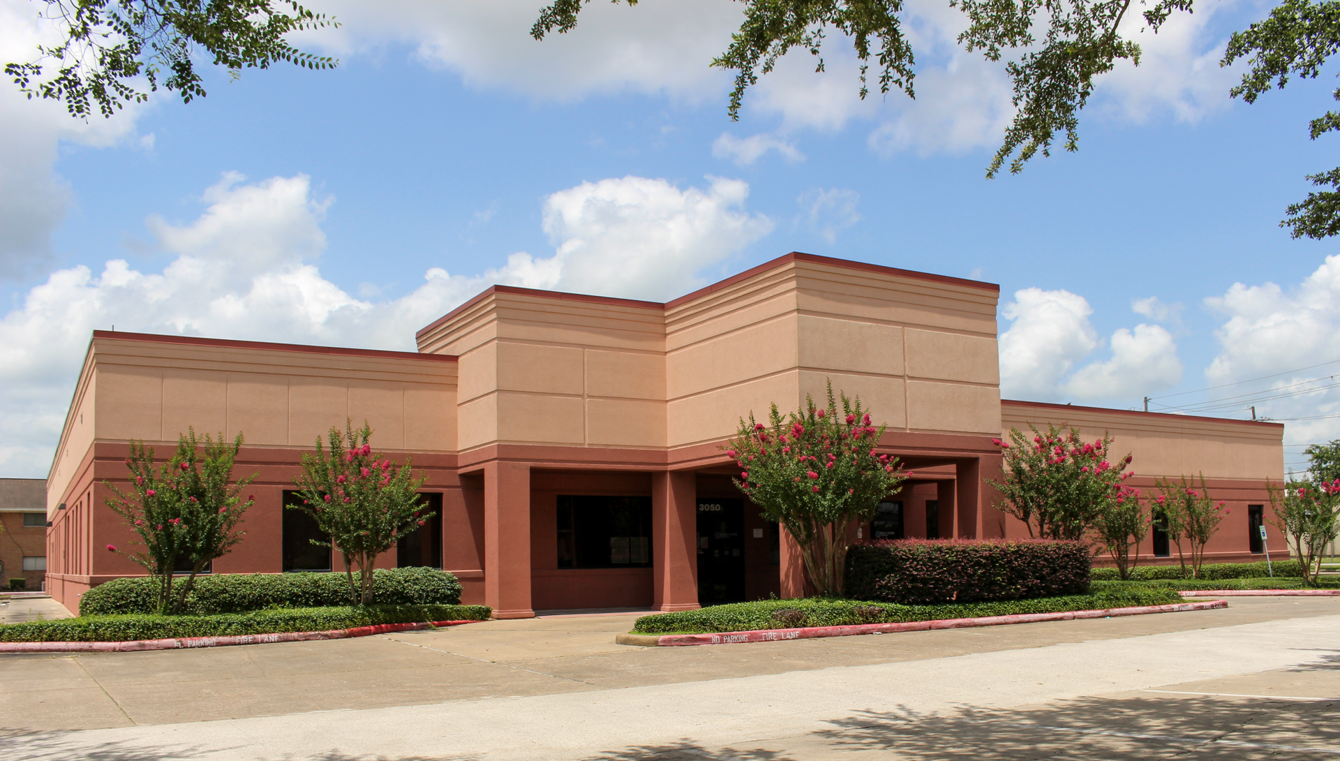 Single tenant DaVita Dialysis building with red trim, seen from the street under a blue sky.
