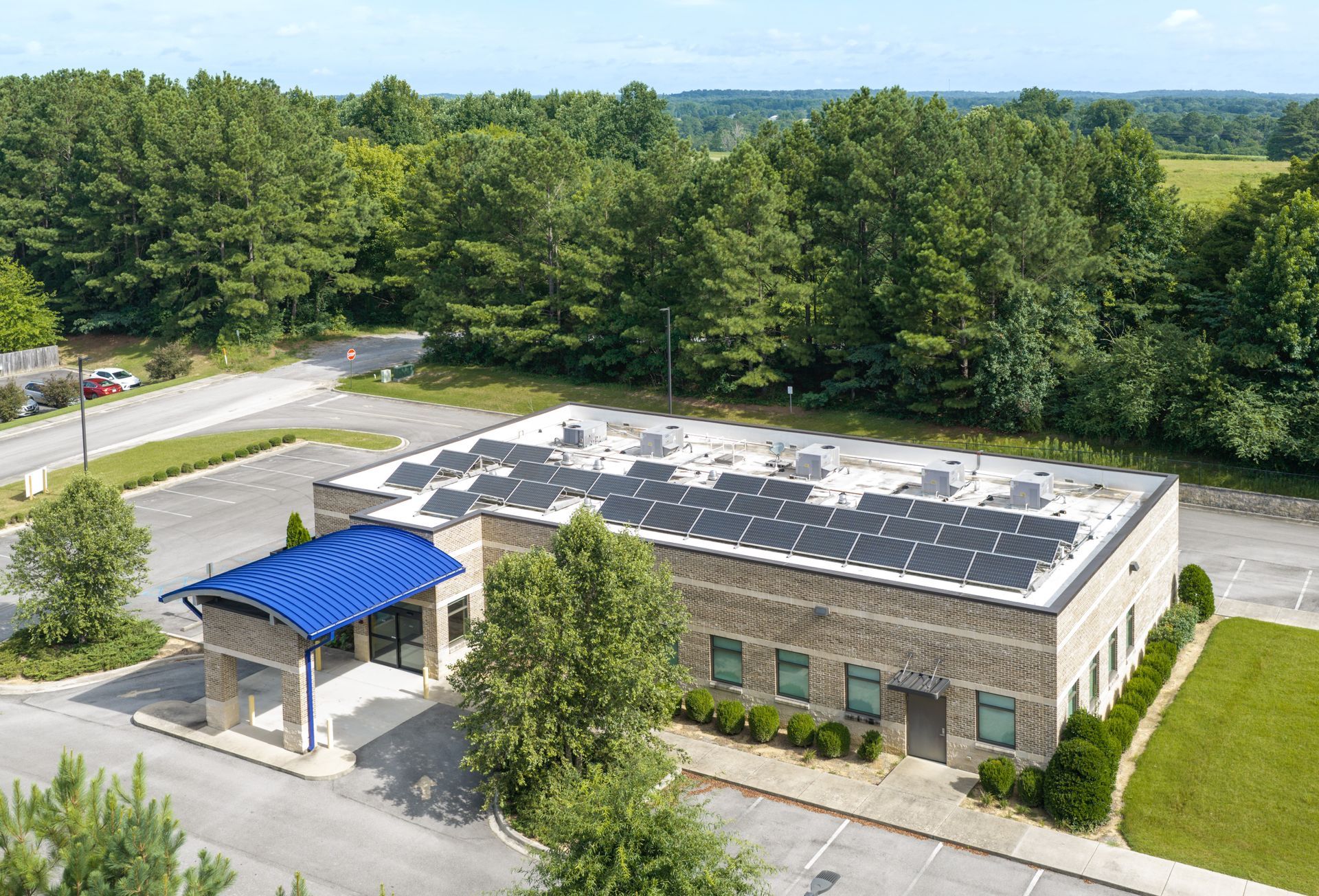 Aerial view of a fresenius kidney care building with a blue entrance awning, surrounded by trees and parking lot