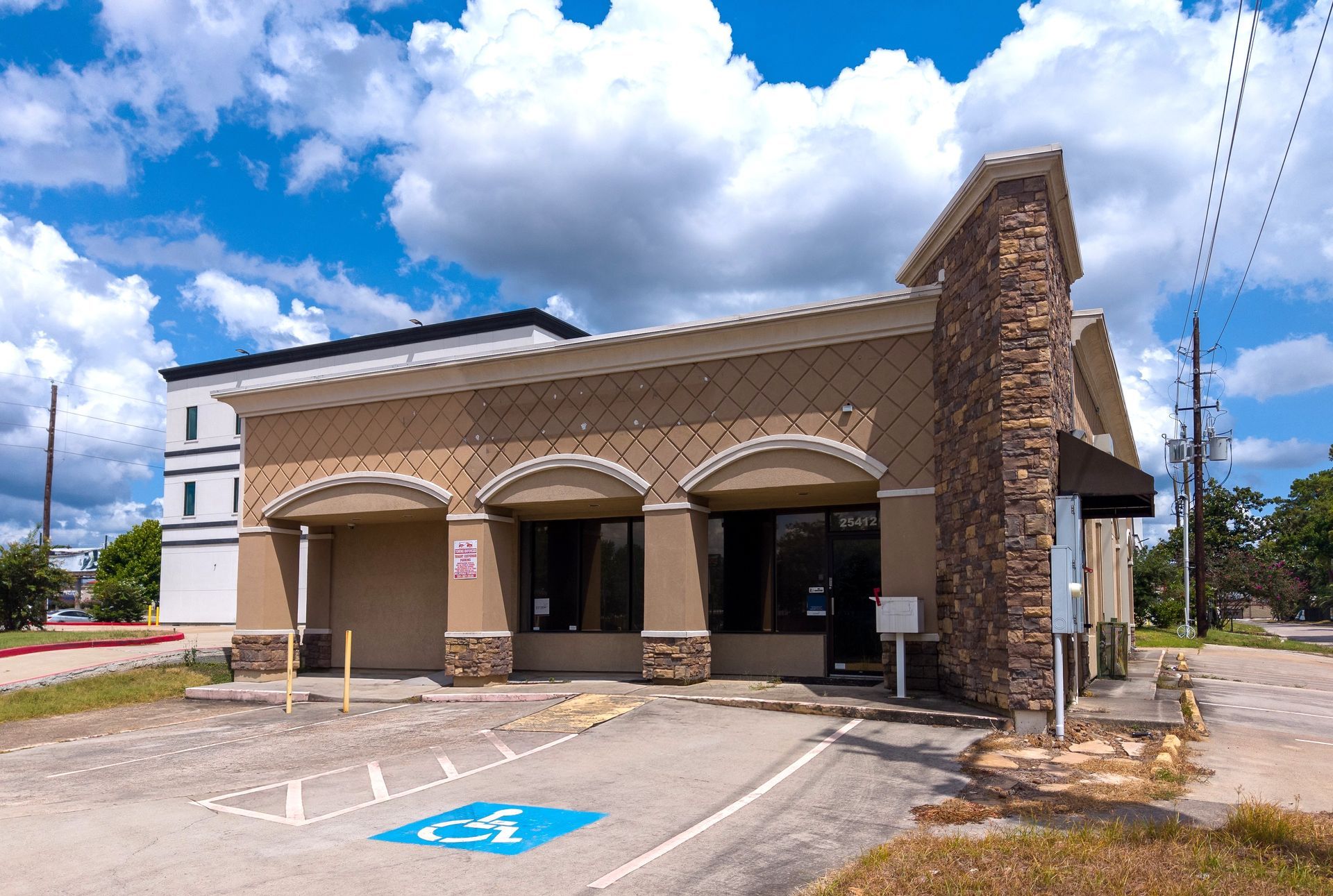 Stone-front drive-thru bank building under a partly cloudy sky, with accessible parking in front