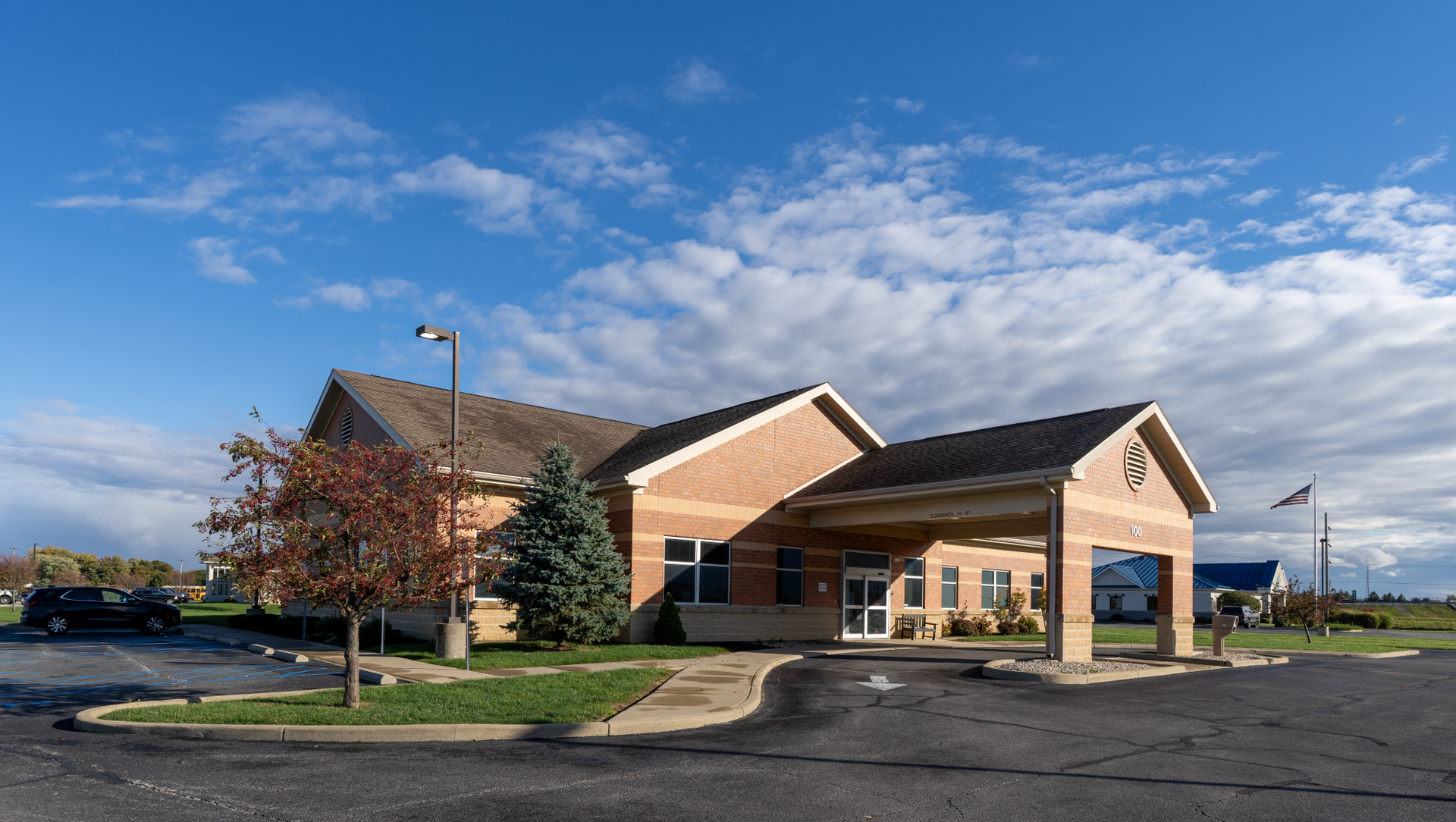 Dialysis center building with covered entrance under a blue sky, trees in front.