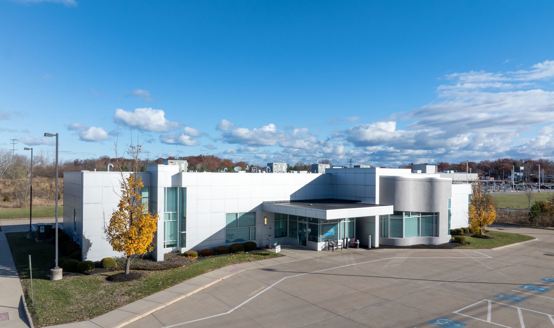 Modern white commercial DaVita Dialysis building with glass entrance, parking lot, and blue sky
