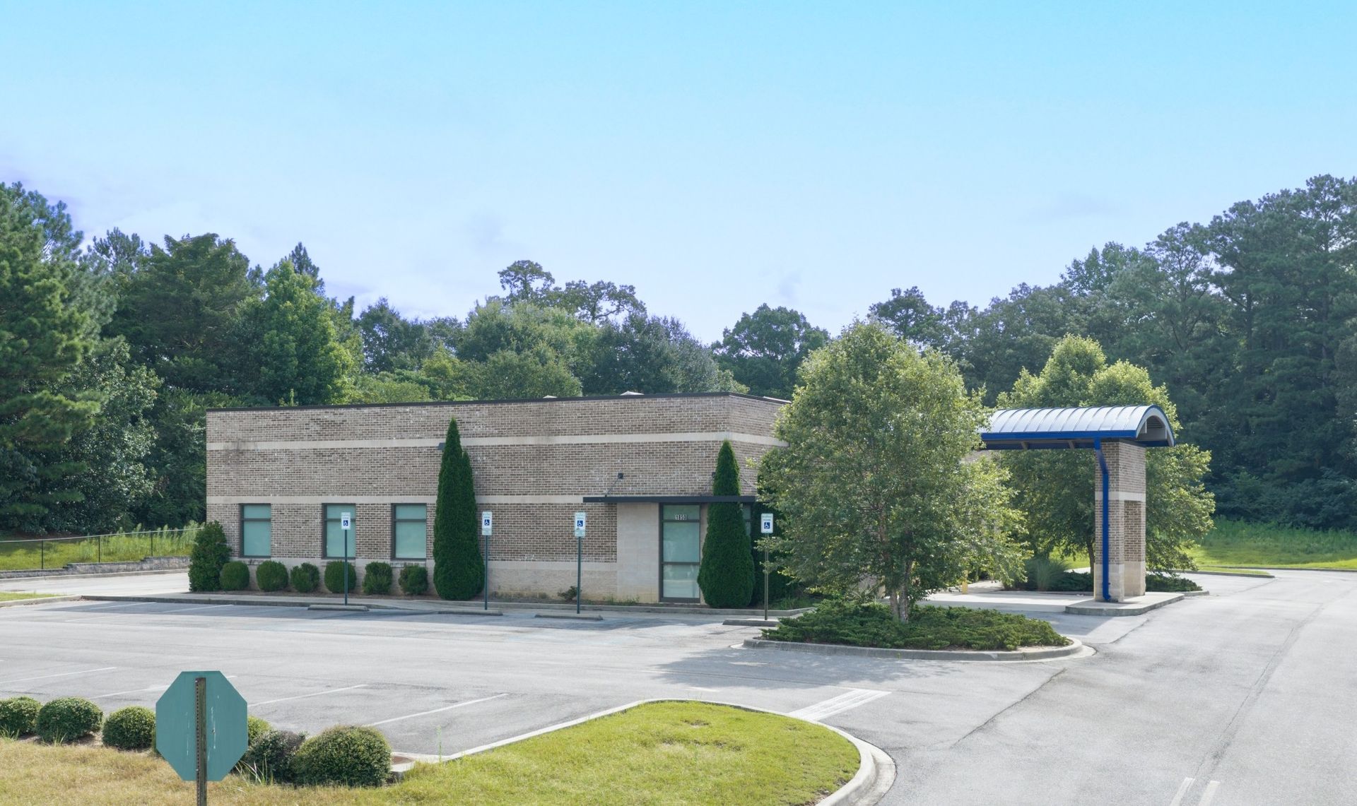 A brick dialysis clinic with a drive-thru canopy beside an parking lot and trees